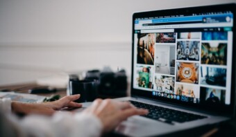 Persona navegando por una galería de fotos en la pantalla de una computadora portátil, accediendo al sitio web, con una cámara y una taza de café también visibles en el escritorio.