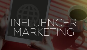 Una persona sostiene una tableta que muestra un ícono de globo terráqueo junto a una taza de café, con el texto superpuesto "Influencer Marketing".