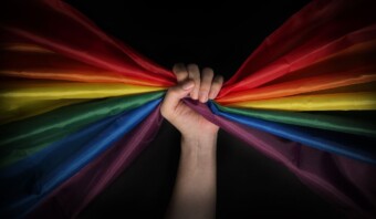 Mano agarrando una tela con los colores del arcoíris sobre un fondo oscuro, que simboliza el orgullo LGBTQ+.