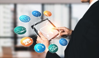Una persona con traje sostiene una tableta con un ícono de carrito de compras en la pantalla. Alrededor de la tableta hay varios íconos que representan diferentes aspectos del comercio electrónico y los negocios digitales, mostrando la perfecta integración de la tecnología en el comercio moderno.