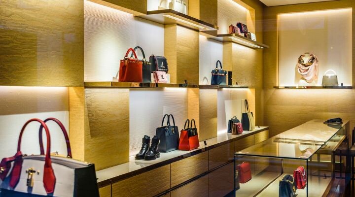 Una exhibición boutique de lujo con bolsos, zapatos y accesorios, junto con elegantes claves, dispuestos en estantes iluminados y dentro de una vitrina de vidrio.