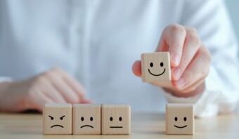 La mano de una persona escogiendo un bloque de madera con una cara feliz de una fila de cuatro bloques con diferentes expresiones faciales, capturando la esencia del marketing emocional.