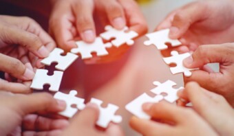 Varias manos sosteniendo piezas de rompecabezas en formación circular, lo que sugiere trabajo en equipo o colaboración.