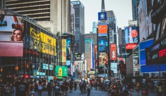 Una concurrida escena callejera en Times Square, ciudad de Nueva York, con brillantes carteles electrónicos que muestran cómo optimizar su mensaje, edificios altos y numerosos peatones.