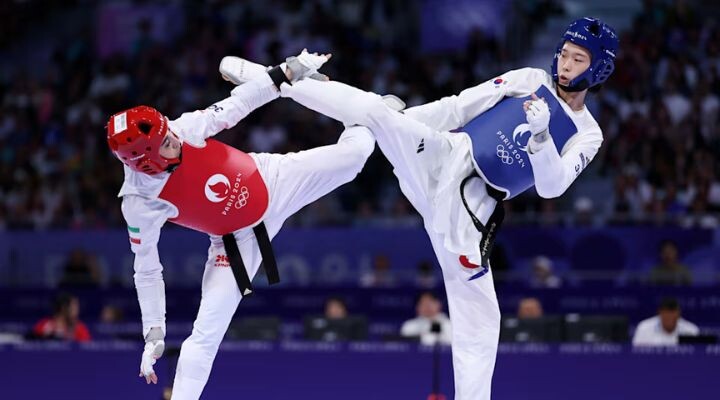 Dos atletas de taekwondo con equipo protector intercambian patadas altas durante un combate, encarnando el espíritu del círculo dorado, uno vistiendo de rojo y el otro de azul.