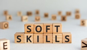 Los bloques de madera dispuestos para deletrear "SOFT SKILLS" sobre una superficie clara enfatizan la importancia de las habilidades blandas, con bloques de letras borrosos adicionales en el fondo.