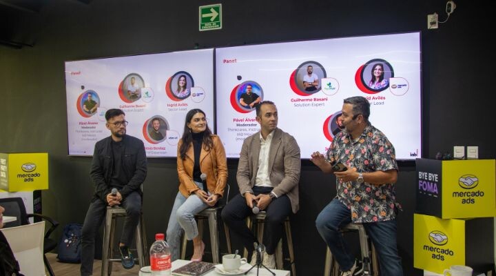 Cuatro personas se sientan en taburetes frente a una pantalla que muestra los perfiles de los oradores, participando en un panel de discusión sobre medios minoristas en un evento de Mercado Ads.