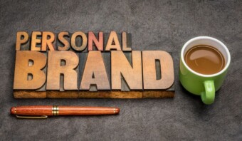 Letras de madera que deletrean "Marcas Personales" junto a una taza de café verde llena de café y un bolígrafo de madera.