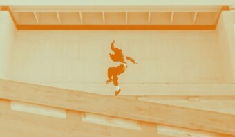 Una figura en el aire realizando un salto en una rampa de hormigón empinada en un entorno abstracto y monocromático de color naranja.