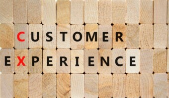 Los bloques de madera deletrean "Experiencia del cliente", con énfasis en "C" y "X" en rojo, resaltando la importancia de CX en el diseño.