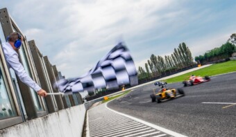 Un oficial de carrera ondea una bandera a cuadros mientras dos coches de Fórmula 1 pasan a toda velocidad por una pista, lo que significa el final de una emocionante carrera en un día nublado.