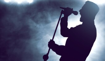 Silueta de un cantante sosteniendo un micrófono en el escenario, que recuerda las actuaciones icónicas de Luis Miguel, con luces brillantes y humo arremolinándose en el fondo.