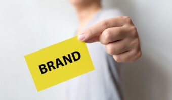 Una persona sostiene una tarjeta amarilla que muestra la palabra "MARCA" en letras negras en negrita, lo que recuerda el concepto de un tablero de marca.