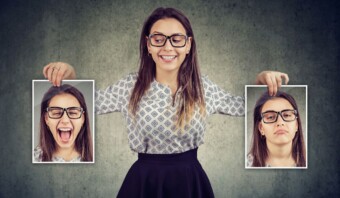 Una mujer sostiene dos fotos de ella misma, una sonriendo y otra frunciendo el ceño, sobre un fondo liso.