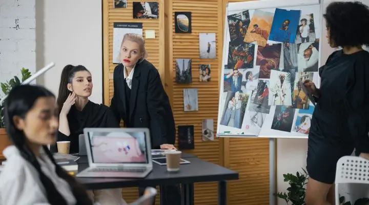 Cuatro personas en una sala de reuniones con un ordenador portátil y tazas de café discuten estrategias de gamificación. Un tablero muestra varias imágenes.