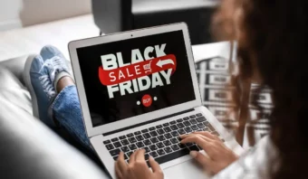 Una persona descansa en un sofá, absorta en su computadora portátil que muestra un anuncio de ofertas del Viernes Negro con un tentador botón "Comprar", que recuerda a las bulliciosas ofertas del Buen Fin.