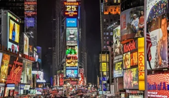 La colorida Times Square por la noche vibra con saturación publicitaria, mientras carteles iluminados y pantallas digitales iluminan la escena, arrojando un brillo vibrante sobre las multitudes que llenan las calles de abajo.