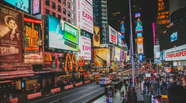 Times Square por la noche estalla con una saturaciÃ³n publicitaria, sus brillantes anuncios y vallas publicitarias iluminan el cielo. La gente camina por la calle, reuniÃ©ndose en este bullicioso centro de intensa energÃ­a.
