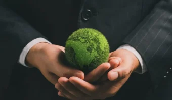 Una persona con traje sostiene un pequeño globo terráqueo cubierto de musgo verde, que simboliza la sostenibilidad y el compromiso con un futuro más verde.
