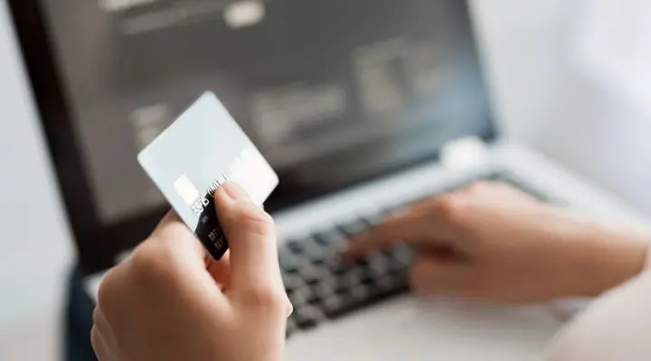 Una persona sostiene una tarjeta de crÃ©dito digital mientras escribe en el teclado de una computadora portÃ¡til.