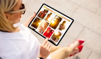 Persona que sostiene una tableta con Pinterest y mira fotografías de mujeres al aire libre. La persona lleva gafas de sol y zapatos rojos.