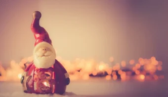 Una pequeña figura de Papá Noel con un fondo brillante de luces cálidas borrosas, colocada sobre la nieve.