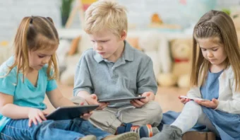 Tres niños sentados en el suelo se concentran en las tabletas en una sala de juegos.