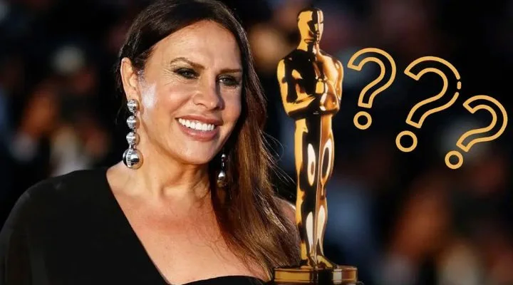 Una mujer con un vestido negro sostiene una estatua de oro con signos de interrogación a su alrededor, sonriendo.