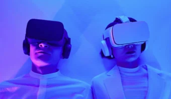 Dos personas vestidas de blanco y con cascos de realidad virtual, tumbadas sobre un fondo iluminado en azul.