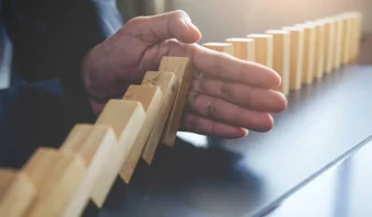 Una mano evita que una fila de fichas de dominó de madera caiga sobre una mesa.