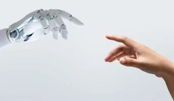 Una mano robótica y una mano humana se extienden una hacia la otra sobre un fondo simple.