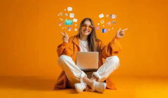 Una persona vestida de color naranja se sienta con las piernas cruzadas con una computadora portátil, rodeada de íconos de redes sociales sobre un fondo naranja, apuntando hacia arriba con ambas manos.