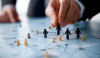 Una mano coloca una figura recortada en un mapa de papel con líneas y figuras, simbolizando la planificación de una red o una estrategia.