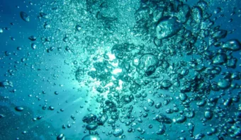 Vista submarina con numerosas burbujas subiendo hacia la superficie contra un fondo de luz solar filtrándose a través del agua.