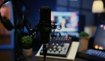 Un primer plano de un micrófono con un filtro antipop en un estudio de grabación, perfecto para podcasting, con auriculares, una consola de mezclas y pantallas de computadora borrosas en el fondo.