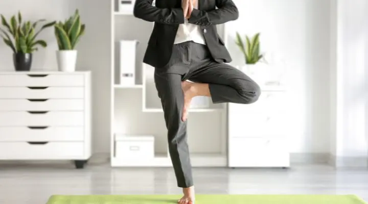 Una persona con traje de negocios realiza una postura de yoga sobre una colchoneta verde en una oficina bien iluminada, representando el equilibrio entre "la ley" y la relajación, rodeada de exuberantes plantas y prístinos estantes blancos.