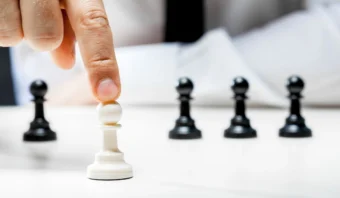 Una mano mueve un peón blanco hacia adelante en un tablero de ajedrez rodeado de peones negros.