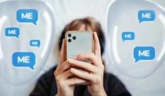 Una persona sostiene un teléfono inteligente, con múltiples burbujas de chat azules que muestran la palabra "YO" a su alrededor.