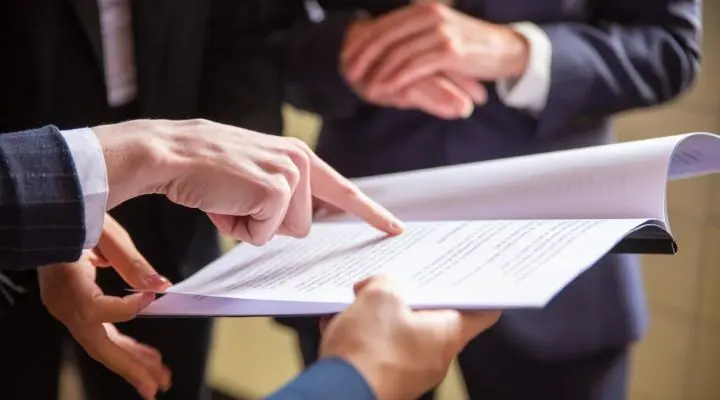 Tres personas vestidas de negocios revisan y discuten un documento, y una de ellas señala una sección específica del Código de ética empresarial.