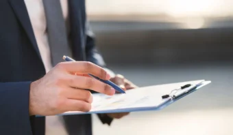 Una persona con traje sostiene un bolÃ­grafo y seÃ±ala un papel con grÃ¡ficos en un portapapeles.