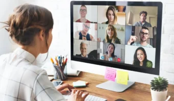 Una mujer se sienta en un escritorio y participa en una videoconferencia con nueve personas, mostradas en una cuadrícula en el monitor de su computadora, mientras sus equipos de trabajo colaboran utilizando el pensamiento de diseño para la innovación.
