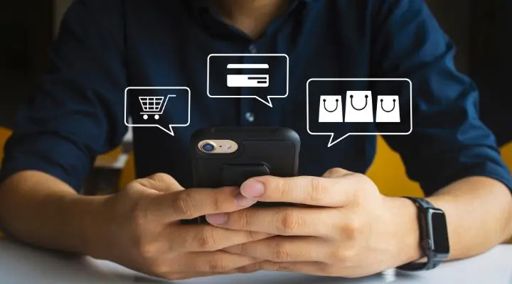 Una persona con una camisa oscura usa un teléfono inteligente con íconos ilustrados de compras, tarjetas de crédito y bolsas de compras flotando sobre la pantalla, reflejando las últimas tendencias en el comercio minorista y retail.