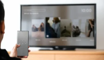 Una persona sostiene un control remoto y lo apunta a un televisor que muestra un menú de servicio de streaming, lo que refleja cómo las tendencias en el comercio minorista influyen en la forma en que consumimos entretenimiento digital.