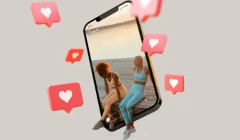 Dos mujeres vestidas con ropa deportiva se sientan en un muelle y aparecen dentro de una gran pantalla de teléfono inteligente con íconos de corazones flotantes, lo que ilustra el poder del marketing de influencia y los “me gusta” de las redes sociales.