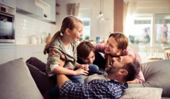 Una familia de cuatro personas se sienta junta en un sofá en una luminosa sala de estar en México, sonriendo y riendo mientras disfrutan de tiempo de calidad juntos.
