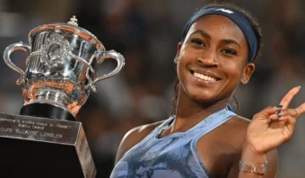 Coco Gauff sonríe y levanta un trofeo con una mano mientras hace un signo de paz con la otra.