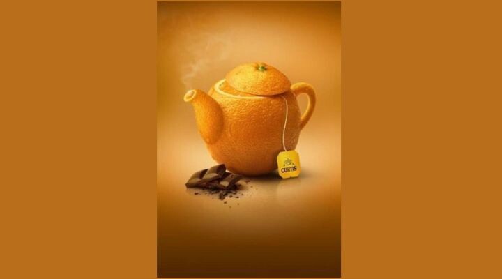 Una tetera encantadora con forma de naranja, de la que sale vapor con gracia, una bolsita de té colgando juguetonamente del pico y tentadores trocitos de chocolate cerca. Esta escena vibrante sobre un fondo naranja resulta tan atractiva como los anuncios cautivadores en un oasis de té relajante. Anuncios publicitarios 