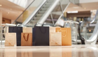 Bolsas de compras creativas descansan en el suelo del centro comercial con escaleras mecánicas que suben en el fondo.