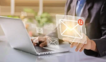 Una persona que usa una computadora portátil con íconos de sobres digitales, uno de los cuales muestra 12 mensajes nuevos, lo que representa la recepción de notificaciones por correo electrónico de campañas de correo electrónico.