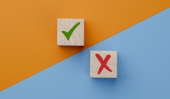 Dos bloques de madera sobre un fondo diagonal naranja y azul; un bloque tiene una marca de verificación verde, el otro tiene una X roja—un aplauso para los errores y los aciertos en cada paso del aprendizaje.